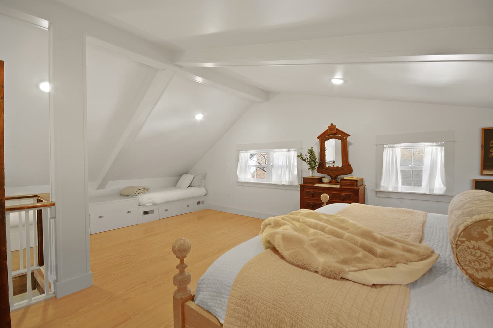 A spacious attic bedroom with a sloped ceiling, light wood floors, a large bed, and a built-in daybed area.