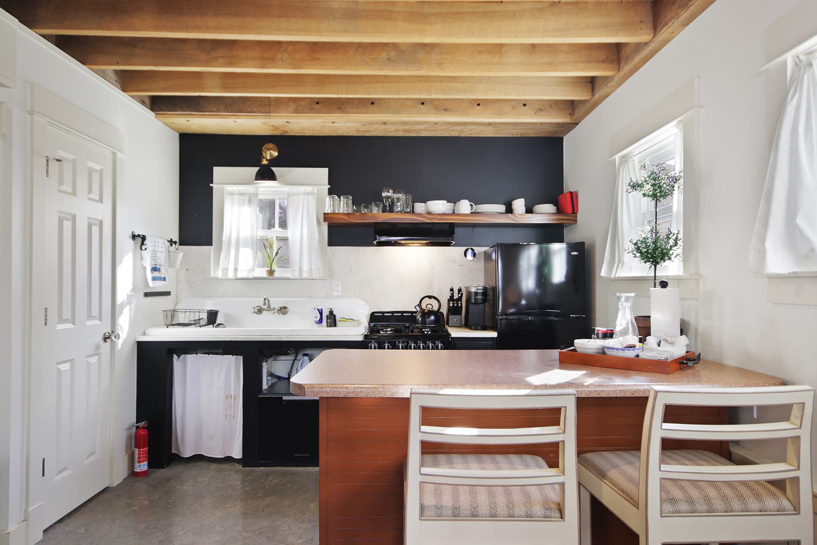 A cozy kitchen with a rustic charm, featuring an exposed wooden beamed ceiling, a dark accent wall, and a wooden island with seating.