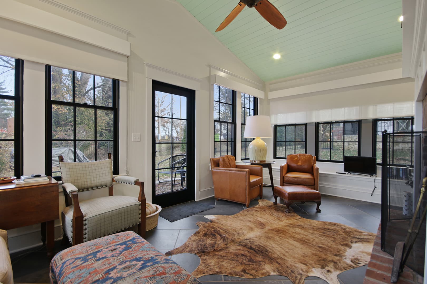 A spacious living area with a vaulted ceiling, large windows with dark frames, and a mix of traditional and rustic furnishings.
