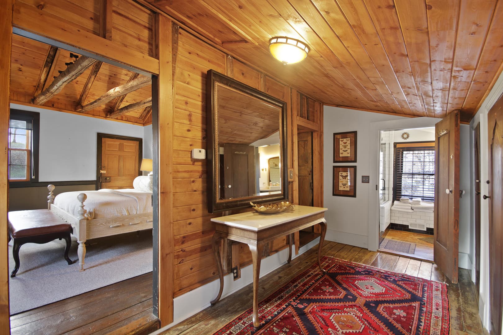 A cozy, rustic interior hallway with wood-paneled walls and ceiling, featuring a console table, a large mirror, and a patterned rug.