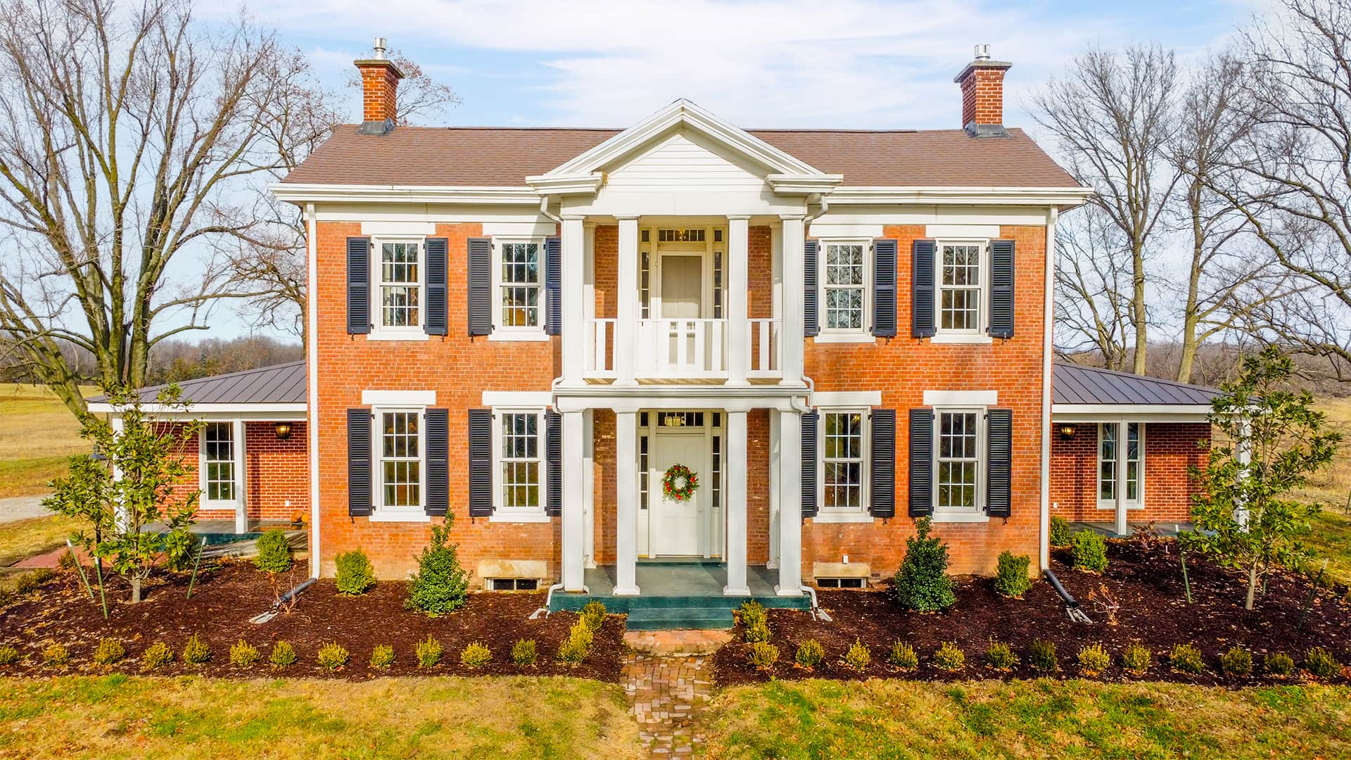 Classic brick mansion surrounded by trees and manicured landscaping.