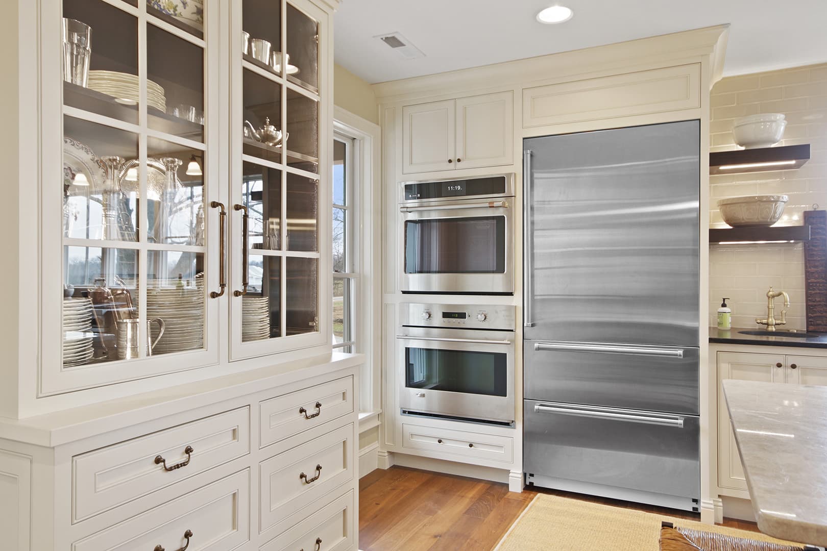 A sophisticated kitchen featuring built-in stainless steel appliances, a large refrigerator, and elegant white cabinetry with glass fronts.