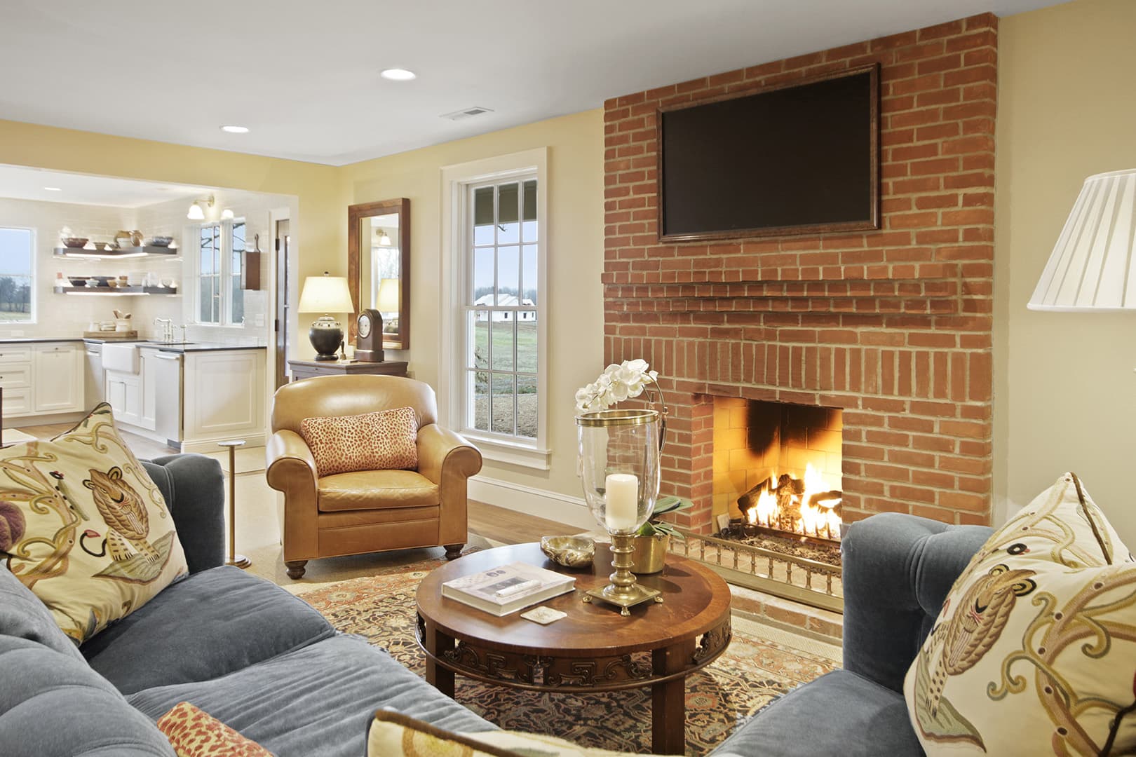Cozy traditional living room with fireplace, leather armchair, plush sofa, and lots of natural light.